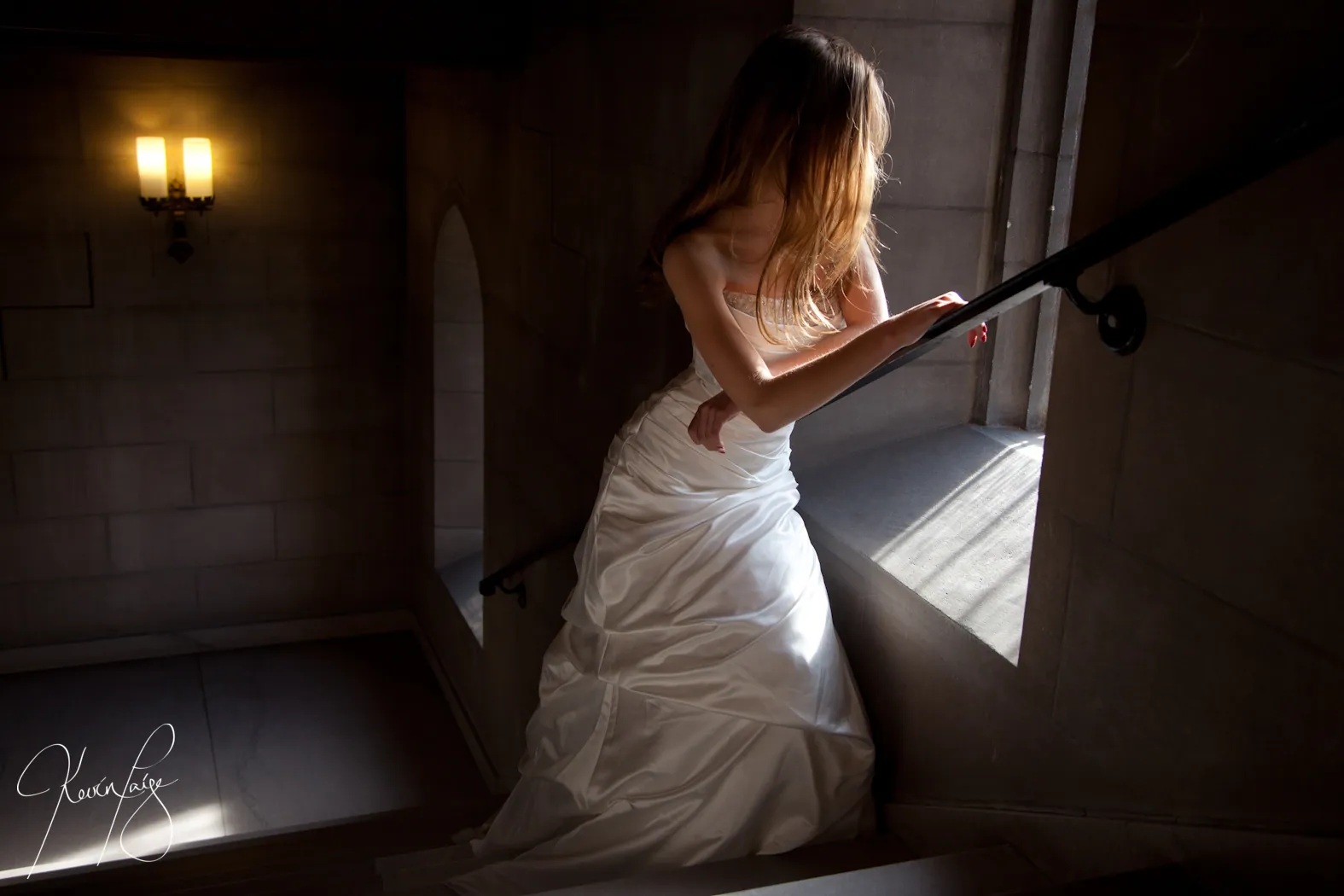 Bride in a white gown at a stone window — natural-light bridal editorial